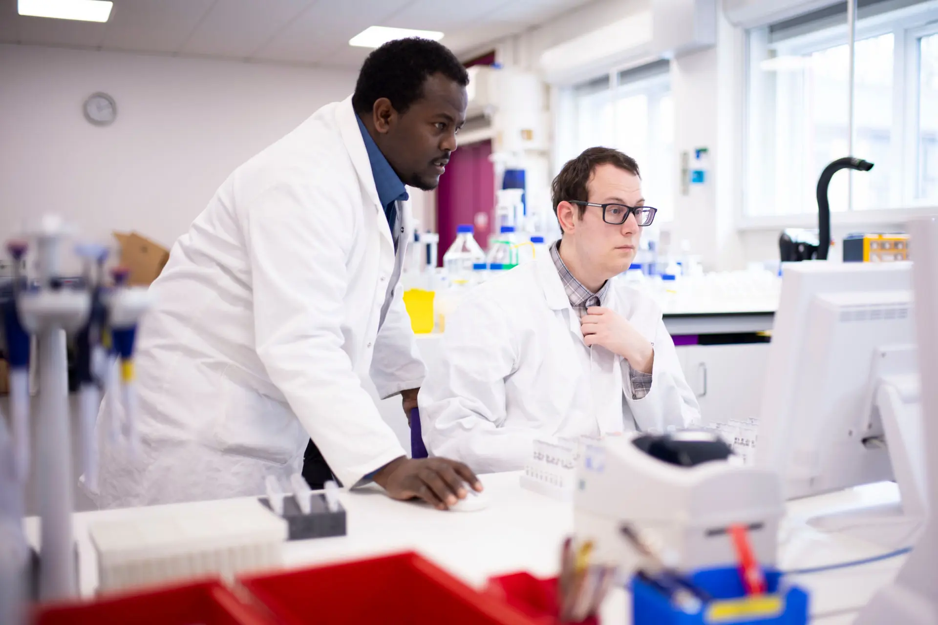Two men wearing lab coats and looking at a computer screen in a laboratory environment