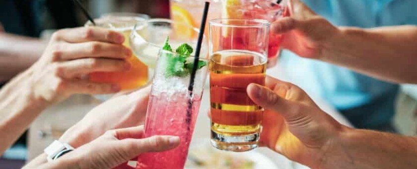 A group of hands holding alcoholic drinks in a 'cheers' motion